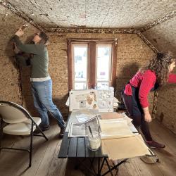 Two conservators examine wallpaper sections.