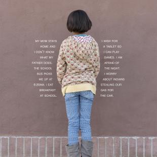 Girl photographed wearing sweater and jeans, facing a wall