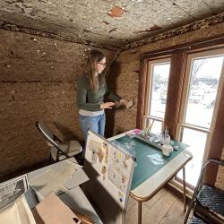 Conservator in the attic bedroom holds a piece of toned paper up against the existing wallpaper.