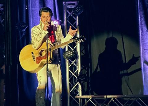 Joseph Hall dressed in white jumpsuit sings into the microphone, as a tribute to Elvis