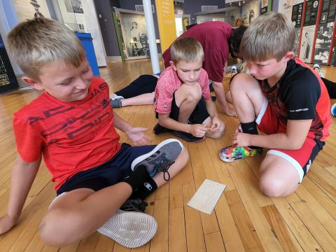 three boys sit on the museum floor deciphering Cather's handwriting