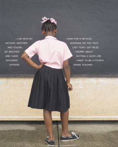 Girl stands facing away from camera in front of chalkboard