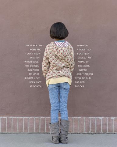 Girl photographed wearing sweater and jeans, facing a wall