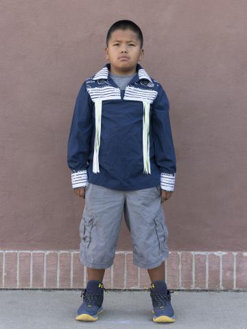 Boy in jacket photographed standing in front of wall